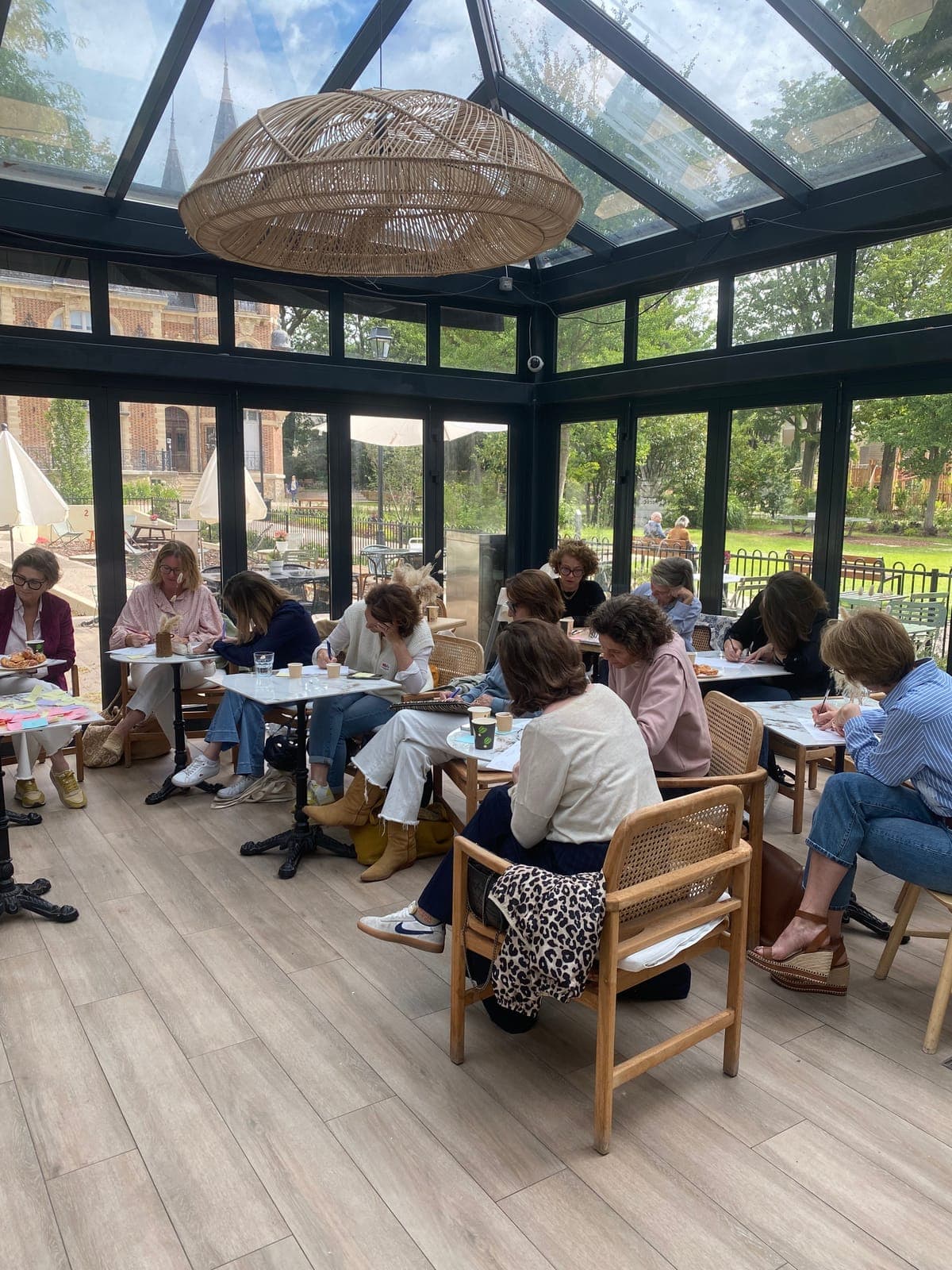 Participantes écrivant à leurs tables sous une grande verrière lors d'un atelier collectif